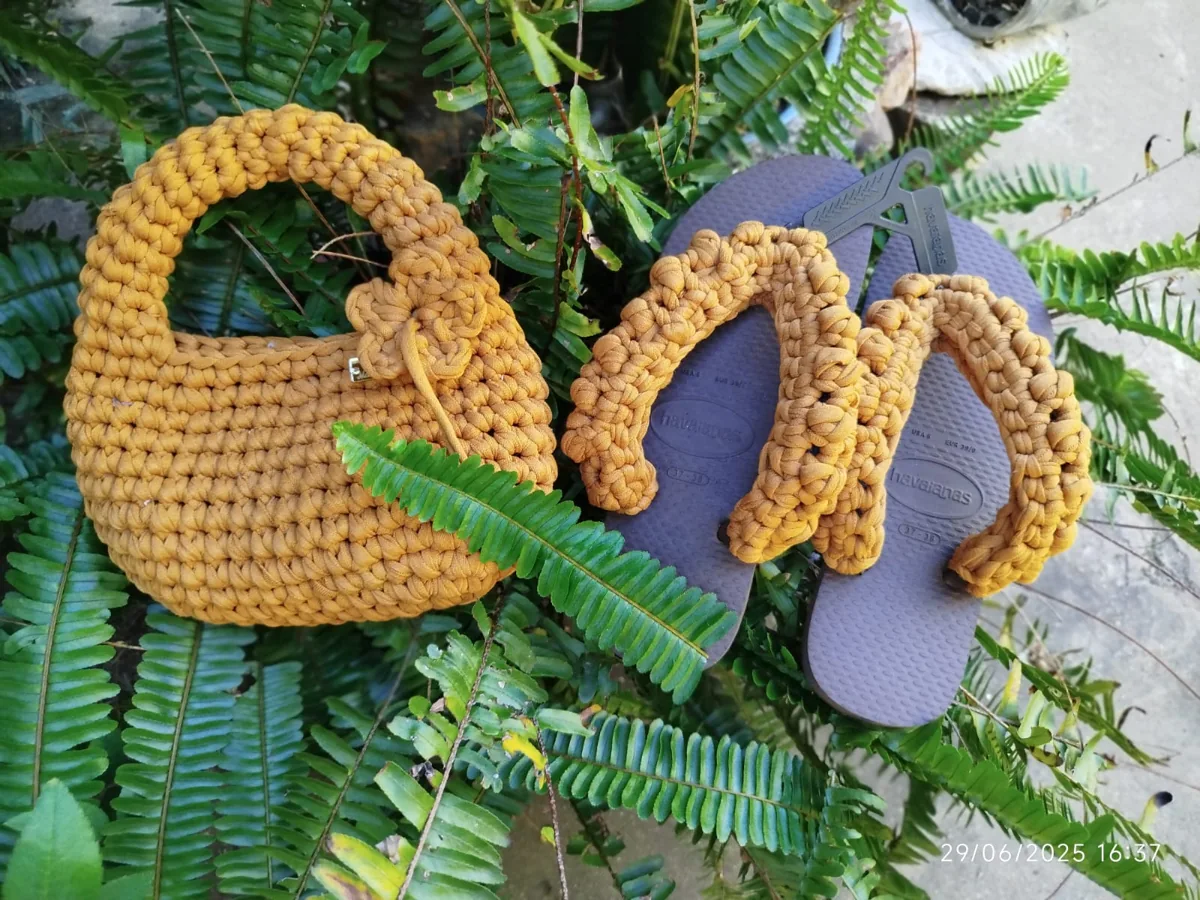 Bolsa e chinelos em tons de mostarda sobre folhas verdes
